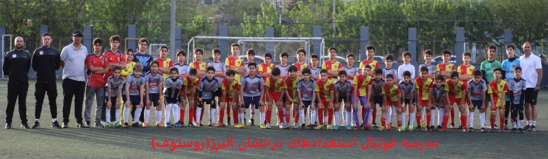 تصویر دوستانه دو تیم نوجوانان بصورت یکی در میان یکی با باس طوسی وآرم روستوف و دیگری قرمز در زمین چمن به همراه مربیان